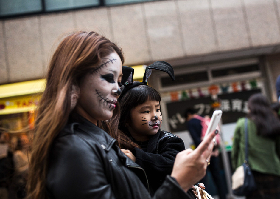 This photo taken October 29, 2016 shows a Japanese woman in a costume checking her smart phone as she carries her daughter during a Halloween parade in Tokyo. PHOTO: AFP
