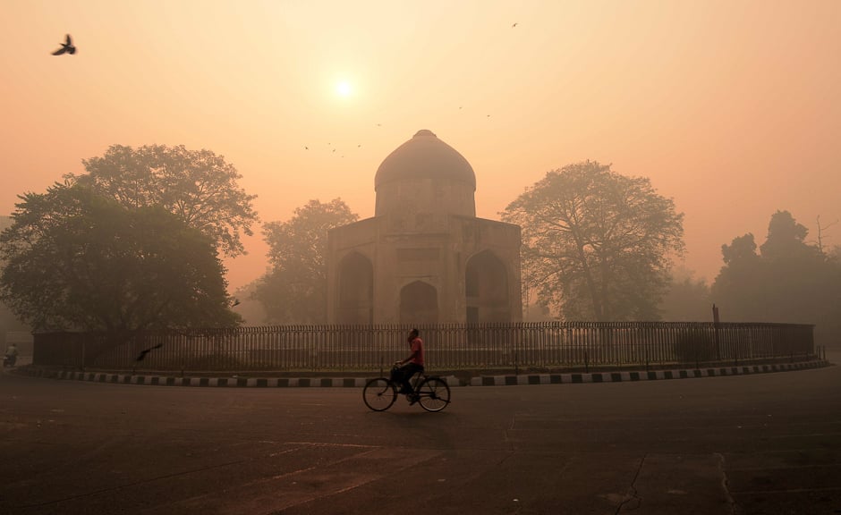 An Indian cyclist rides along a street as smog envelops a monument in New Delhi on October 31, 2016, the day after the Diwali festival. PHOTO: AFP