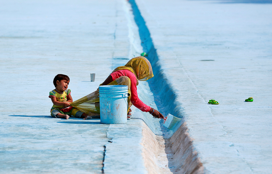 A woman paints the floor of a pond as her child pulls at her saree in Delhi, India. PHOTO: REUTERS