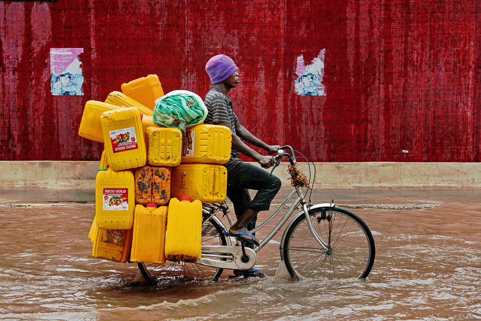 A man bicycles down a flooded street with empty cooking oil containers during a rain storm in Dar es Salaam, Tanzania. PHOTO: AFP