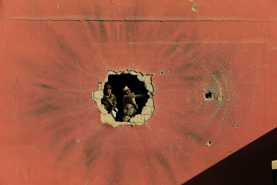 Policemen look through a hole in a house from the clashes in Qaraqosh, near Mosul, Iraq. PHOTO: REUTERS