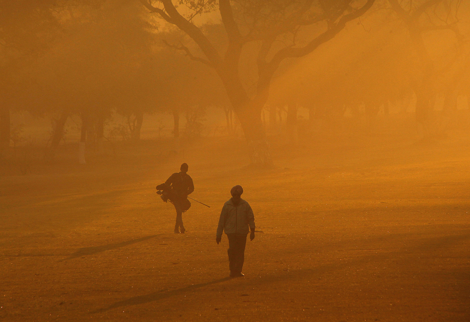 A golfer and his caddie walk on a driving range amid fog during a cold winter morning in Chandigarh, India. PHOTO: REUTERS