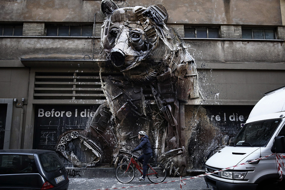 A man rides his bike past a bear made from recycled materials on the facade of the 