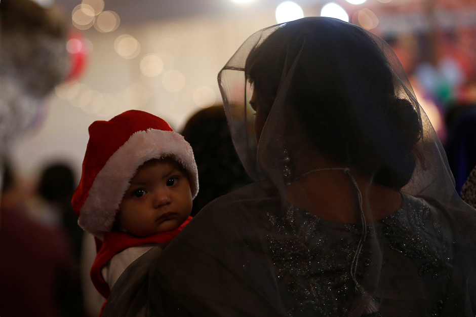 A woman holds a baby in Santa Claus cap, as they attend a ceremony with others on Christmas eve at Central Brooks Memorial Church in Karachi. PHOTO: REUTERS