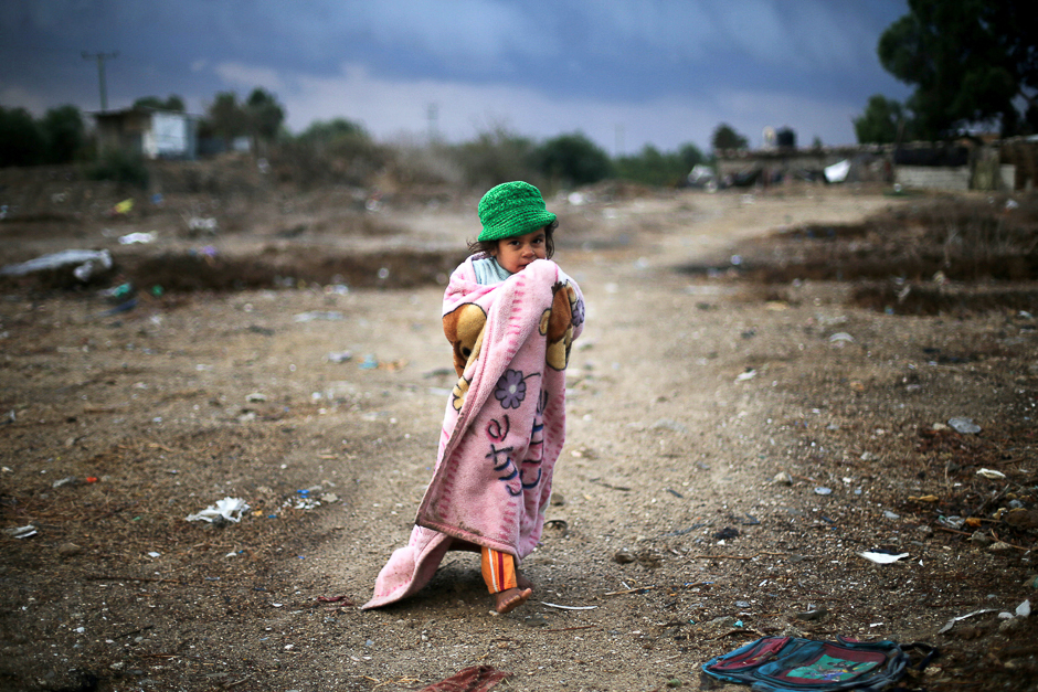 A Palestinian girl, wrapped in a blanket, walks outside her family dwelling on a rainy day in Khan Younis in the southern Gaza Strip. PHOTO: REUTERS
