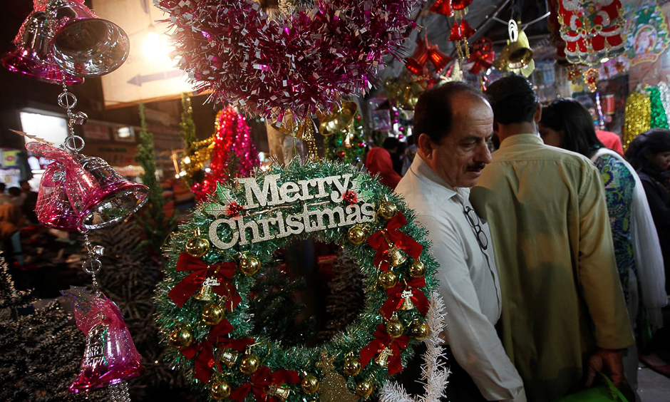 People walk past an artificial decoration wreath hanging outside a shop selling various items for Christmas celebrations in Karachi, Pakistan, December 24, 2016. REUTERS/Akhtar Soomro