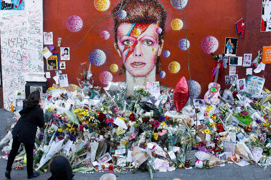 A woman looks at floral tributes placed in front of a mural of British singer David Bowie, painted by Australian street artist James Cochran in Brixton, south London on January 15, 2016. PHOTO: AFP