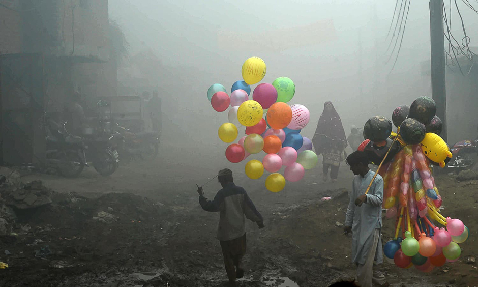 TOPSHOT - Pakistani balloon vendors cross a street in heavy fog in Lahore on December 24, 2016. / AFP PHOTO / ARIF ALI