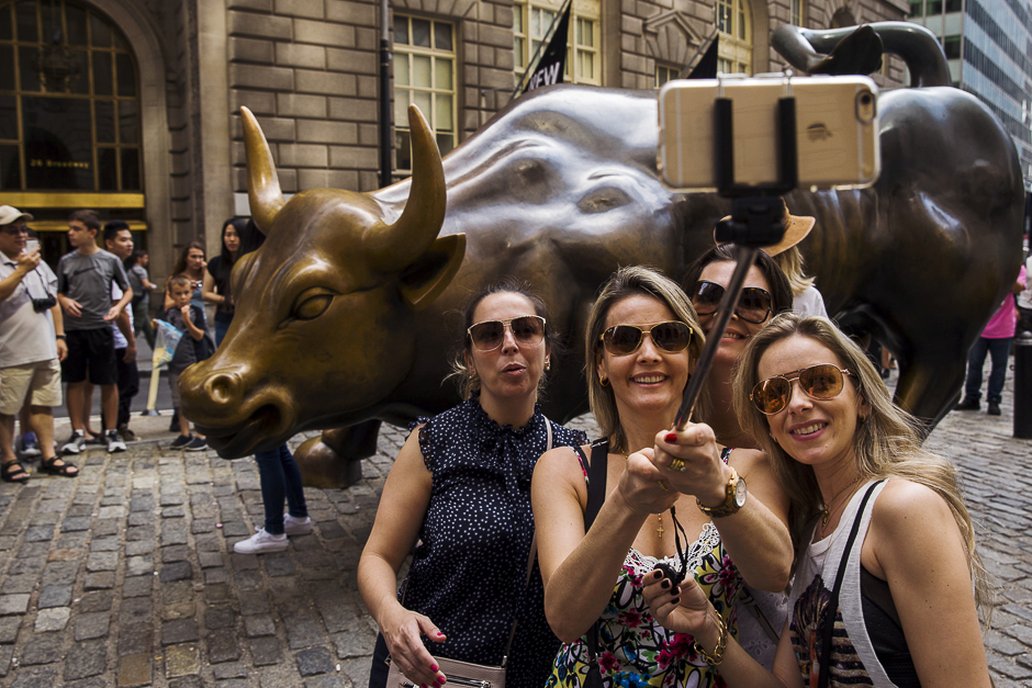 Tourists pose for photographs with a landmark statue of a bull in New York. Wall Street opened sharply lower on Monday with the Dow Jones industrial average losing more than a 1,000 points following a more-than 8 percent drop in Chinese shares and a selloff in oil and other commodities. PHOTO: REUTERS