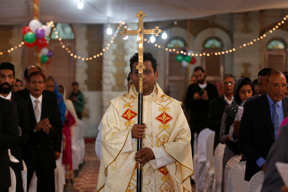 A member of church holds a cross as he walks past people pray during a ceremony on Christmas eve at Central Brooks Memorial Church in Karachi. PHOTO: REUTERS