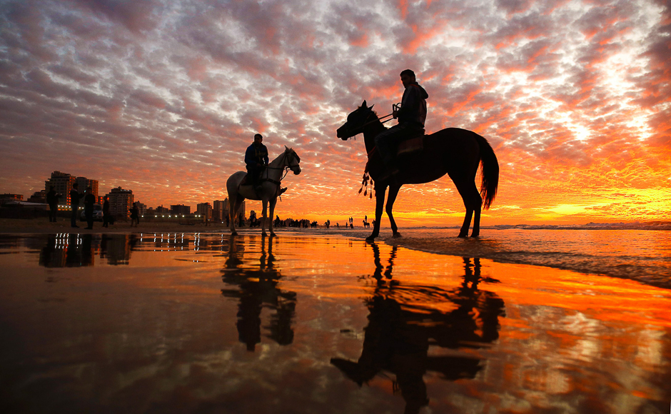 Palestinians ride horses on the beach as the sun sets over Gaza City. PHOTO: AFP