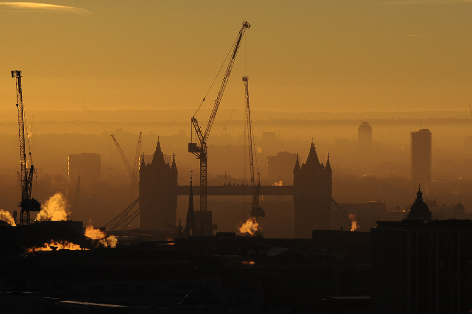 Construction cranes are pictured near Tower Bridge in London at sunrise. PHOTO: AFP