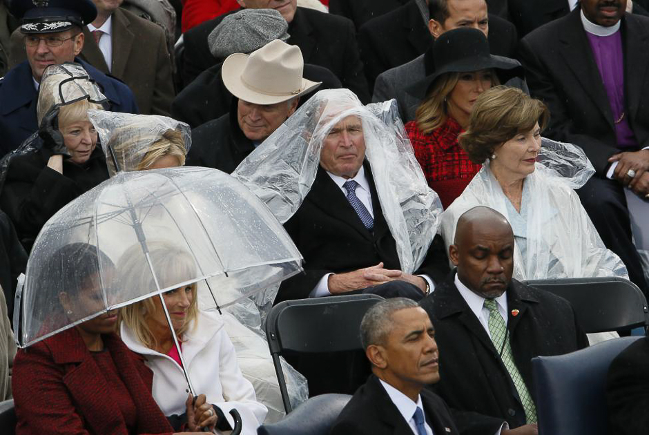 Former president George W. Bush keeps covered in the rain as he sits with his wife Laura. 