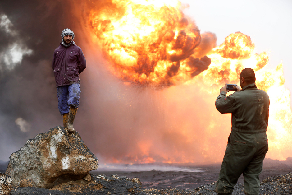 A man takes a photograph of his friend as thick smoke rises from a fire, which broke out at oil wells set ablaze by Islamic State militants before they fled the oil-producing region of Qayyara, Iraq. PHOTO: REUTERS