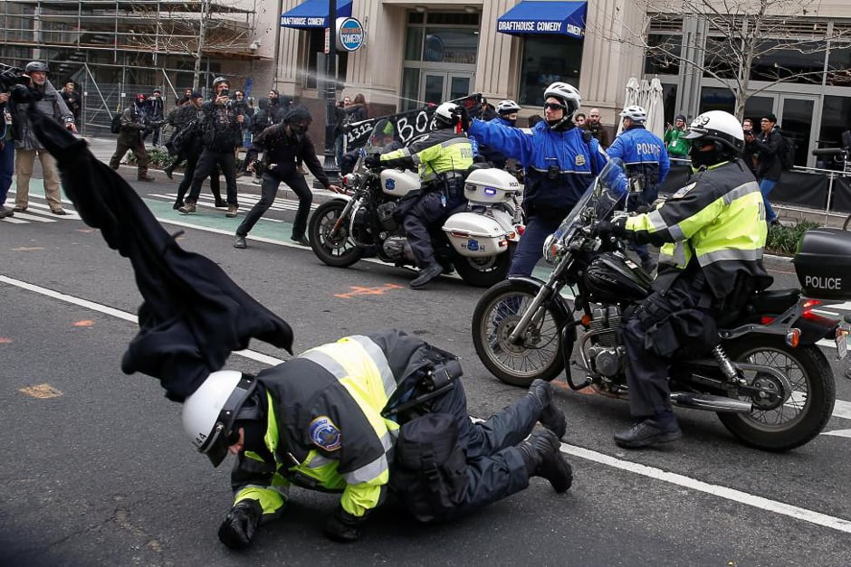 A police officer falls to the ground as another shoots pepper spray at protesters demonstrating against Trump on the sidelines of the inauguration. PHOTO: REUTERS