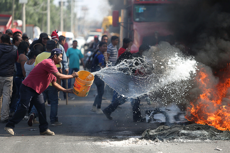 A man throws water on burning tires during a protest against the rising prices of gasoline enforced by the Mexican government at the side of a Pemex gas station in San Miguel Totolcingo , Mexico. PHOTO: REUTERS