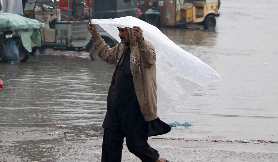 A man uses a plastic sheet to protect himself during the rain. PHOTO: ONLINE/SABIR MAZHAR