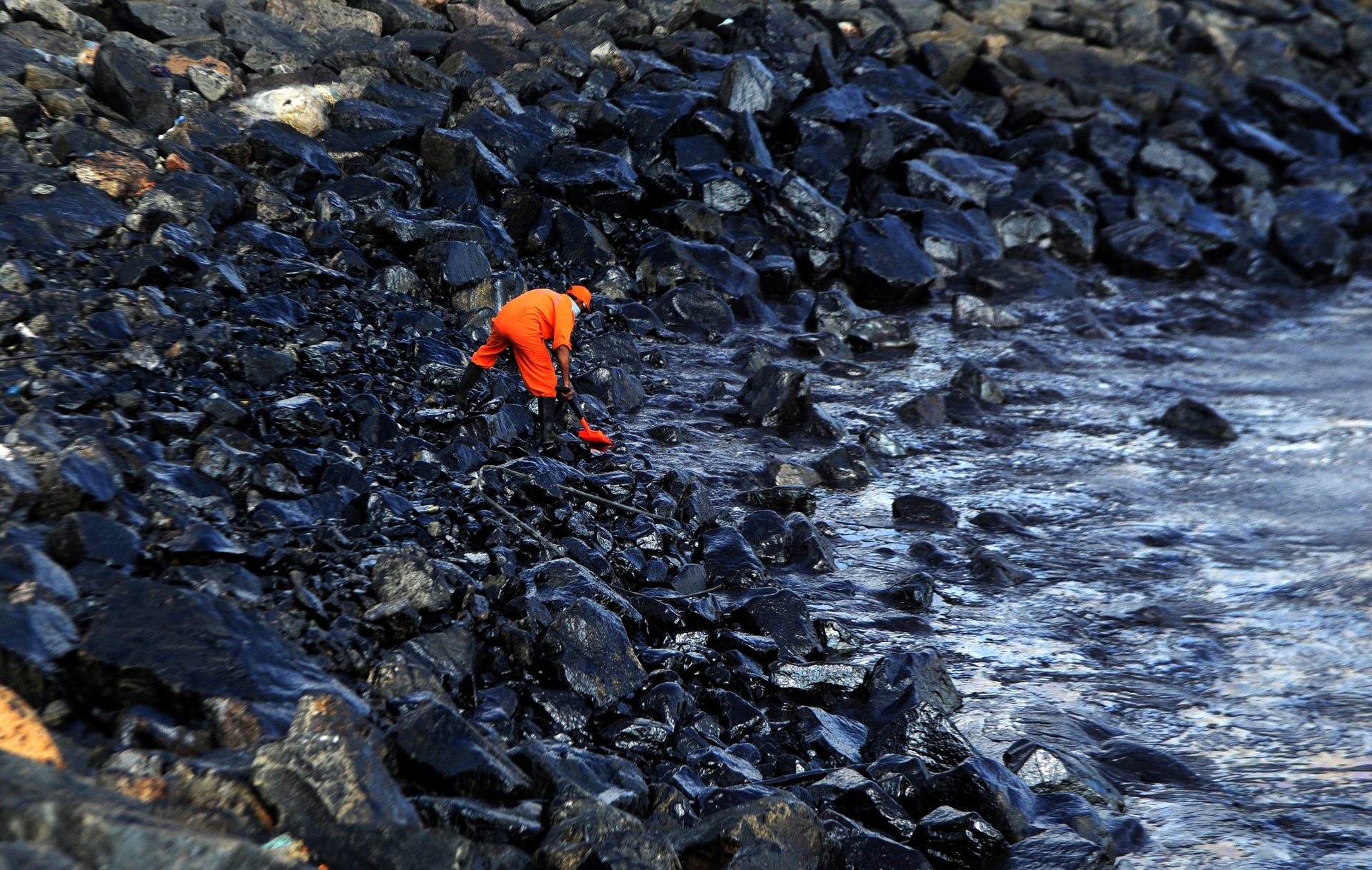 A member of the pollution response team collects a sample of the oil covering rocks at the sea edge after a spillage when two tankers collided off Kamarajar Port, Chennai, India. PHOTO: AFP