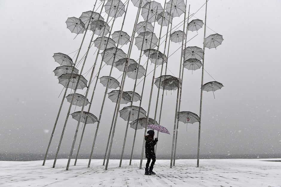 A woman holding an umbrella walks under Greek sculptor artist George Zongolopoulos' 'Umbrellas,' during heavy snowfall in Thessaloniki. PHOTO: AFP
