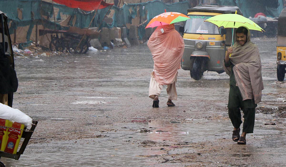 Locals carry umbrellas to protect themselves from rain in the port city. Rain water is seem accumulated on a road near Tower. PHOTO: ONLINE/SABIR MAZHAR