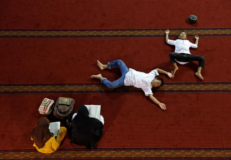 INDONESIA: Women read the Koran as boys rest inside Istiqlal mosque during the holy month of Ramadan in Jakarta, Indonesia June 9, 2016. REUTERS/Beawiharta