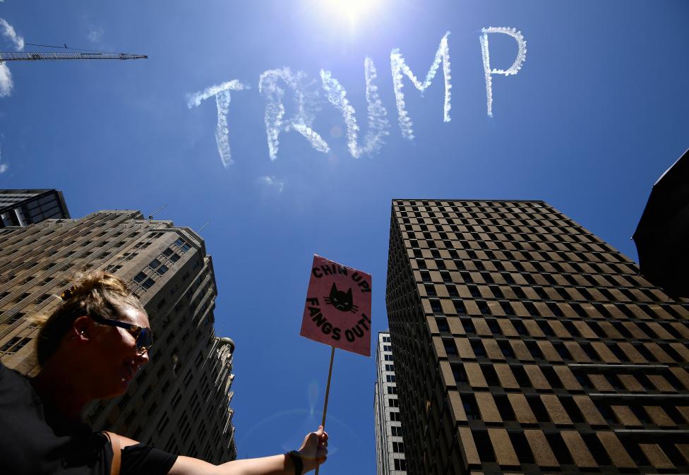 The name of U.S. President Donald Trump can be seen in the sky above a protester as she carries a sign during the first of hundreds of womens' marches organized around the world in a show of disapproval of the new President in Sydney, Australia. AAP/Dan Himbrechts/via REUTERS