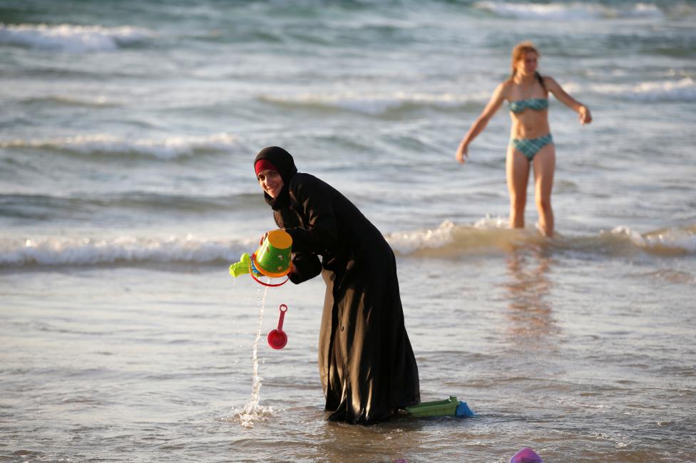 ISRAEL: A Muslim woman wearing a Hijab stands in the waters in the Mediterranean Sea as an Israeli stands nearby on the beach in Tel Aviv, Israel August 21, 2016. REUTERS/Baz Ratner