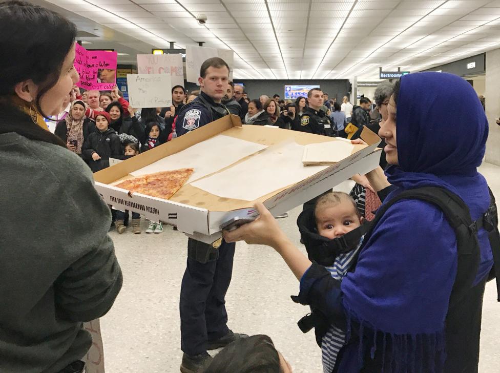 A woman offers pizza to people protesting against the travel ban imposed by U.S. President Donald Trump's executive order, at Washington Dulles International Airport in Dulles. REUTERS/Yeganeh Torbati