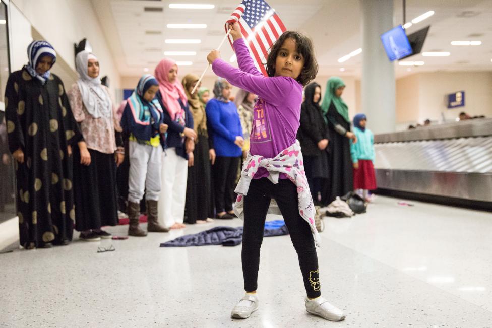 A young girl dances with an American flag in baggage claim while women pray behind her during a protest against the travel ban imposed by U.S. President Donald Trump's executive order, at Dallas/Fort Worth International Airport in Dallas. REUTERS/Laura Buckman