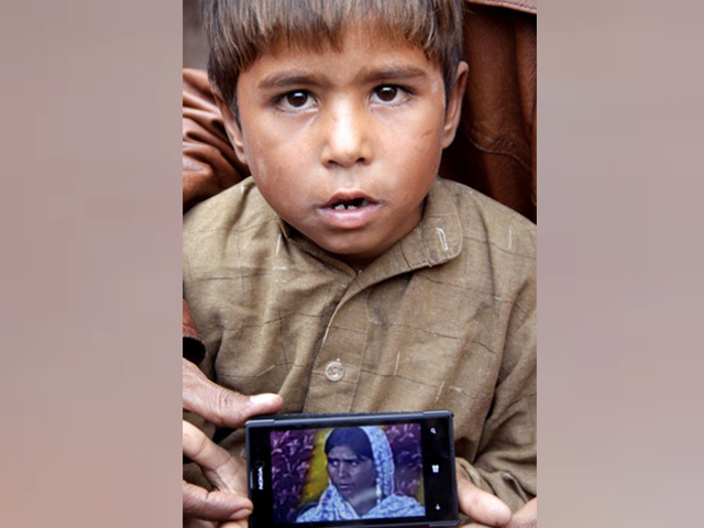 Suleman, son of Shama and Shehzad, holds up a photo of his mother on a phone. PHOTO: SHAFIQ MALIK/EXPRESS