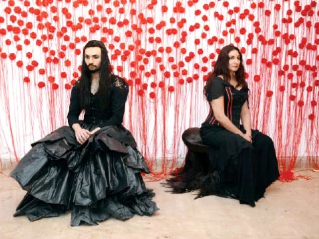 Muhammad and Manizhe Ali sat in mourning wearing black with a backdrop of a wall covered in roses made of yarn. The piece was dedicated to the children who had lost their lives in Tuesday’s militant attack. PHOTO: COURTESY AMIN GULGEE GALLERY
