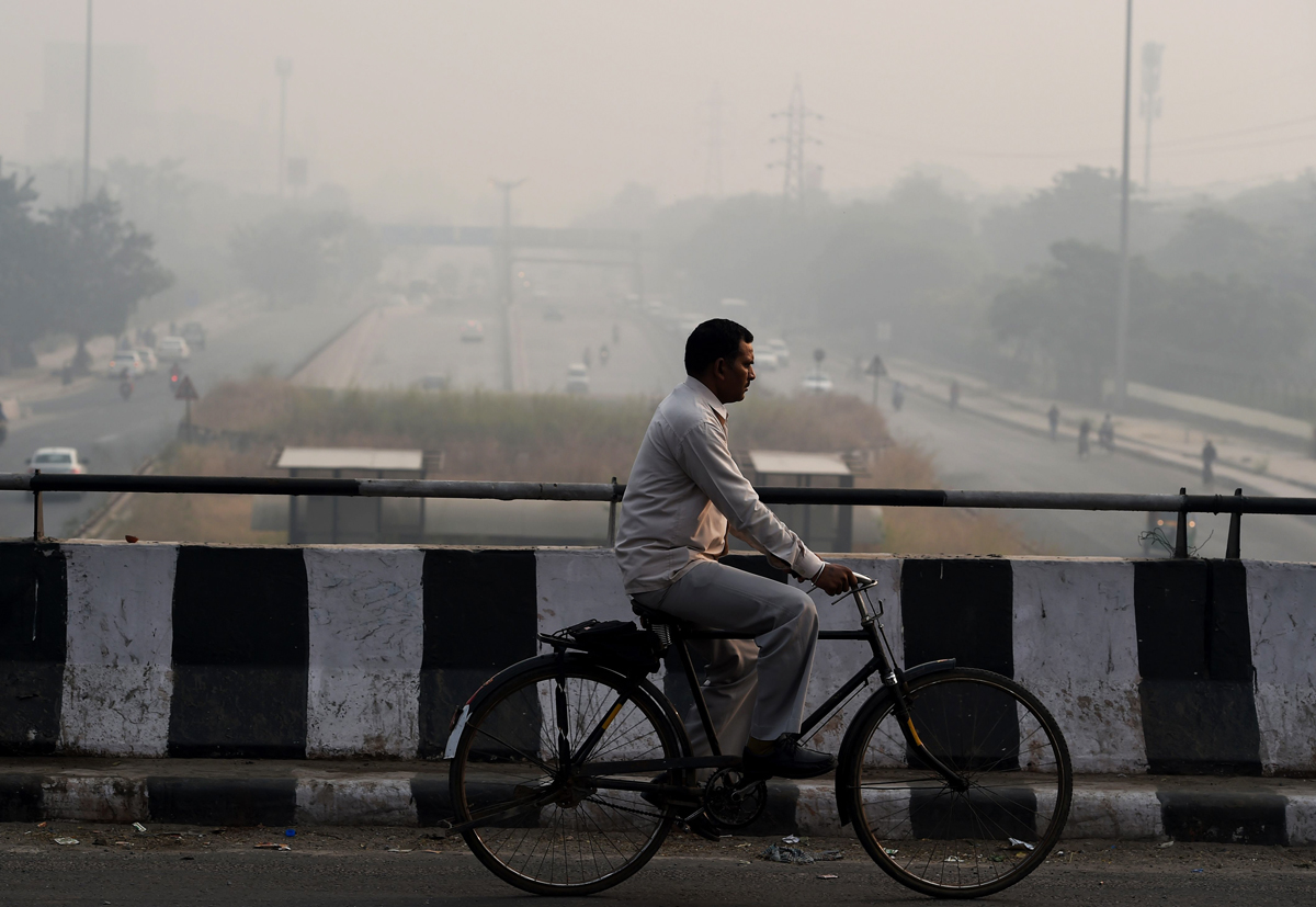 an indian cyclist rides over a bridge as smog envelopes new delhi on october 31 2016 the day after the diwali festival photo afp