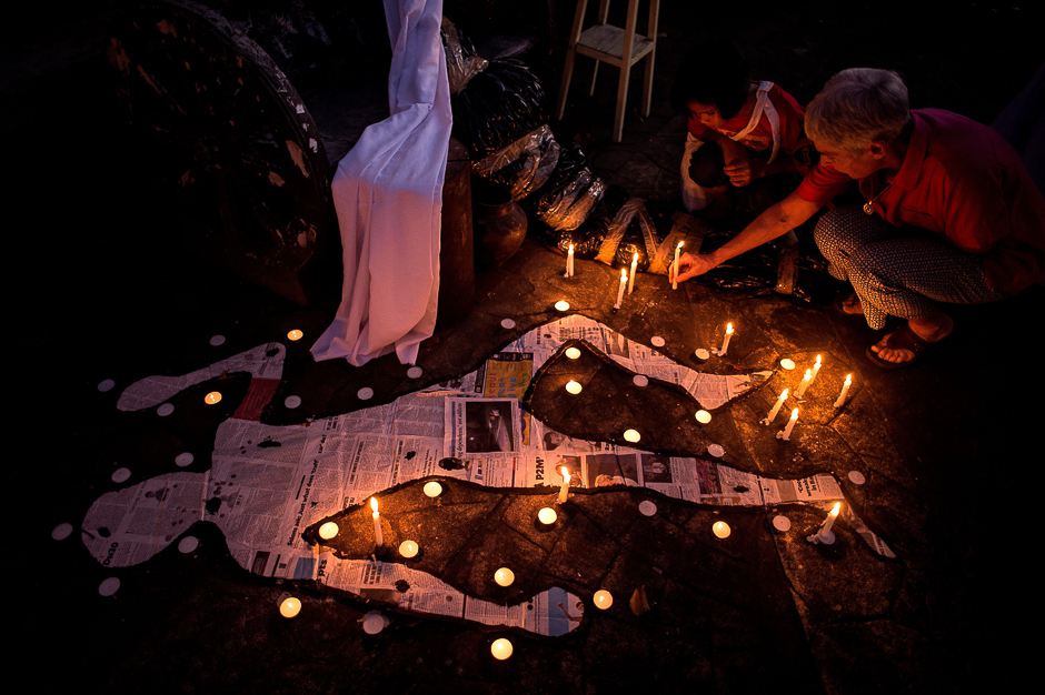 A catholic devotee and her grandchild lights a candle beside mock chalk figure representing an extra judicial killing victim during a prayer rally condemning the government's War on Drugs in Manila. PHOTO: AFP