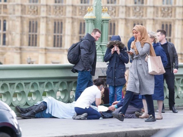 A hijab-clad woman walks past a group of people helping a victim. PHOTO: TWITTER