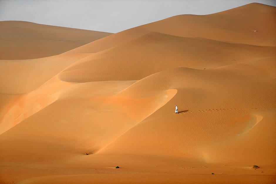 Emirati men walk across the dunes in the Rimah desert, west of Al-Ain in the United Arab Emirates. PHOTO: AFP