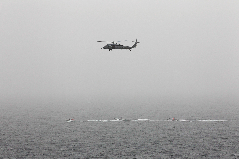 Three Iranian Revolutionary Guard boats are seen near the US aircraft carrier, USS George H. W. Bush while transiting Straits of Hormuz as US. Navy helicopter hovers over them during early hours. PHOTO: REUTERS