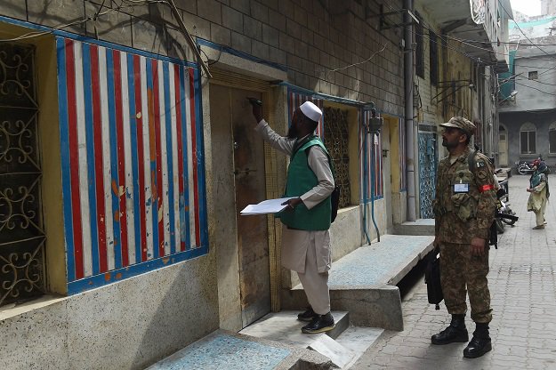 An official from the Pakistan Bureau of Statistics (L) marks a house after collecting information from a resident during a census as army slodier stands guard in Lahore on March 15, 2017. PHOTO: AFP