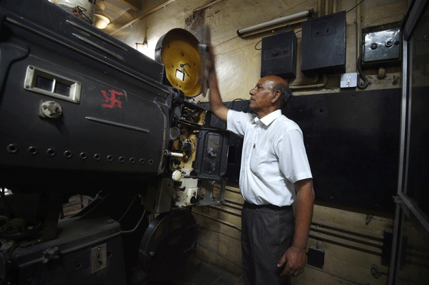 This picture taken on March 27, 2017 shows Indian projectionist Ramesh Kumar, who has worked at the Regal cinema for 23 years, looking at an old projector at the 84-year-old movie hall in the heart of the Indian capital New Delhi. PHOTO: AFP