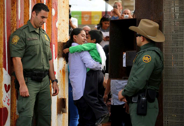 US Border patrol agents stand at an open gate on the fence along the Mexico border to allow Luis Eduardo Hernandez-Bautista hug Ty'Jahnae Williams and his father Eduardo Hernandez (not in view), as part of Universal Children's Day at the Border Field State Park, California, US on November 19, 2016. PHOTO: REUTERS