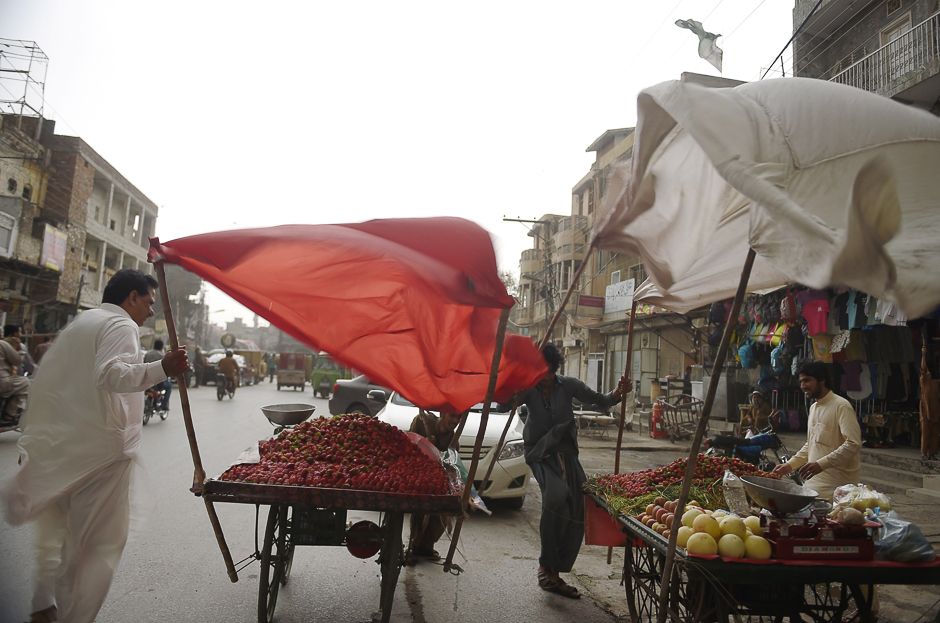 Pakistani fruit vendors try to control sunshades during high winds at a market in Rawalpindi. PHOTO: AFP