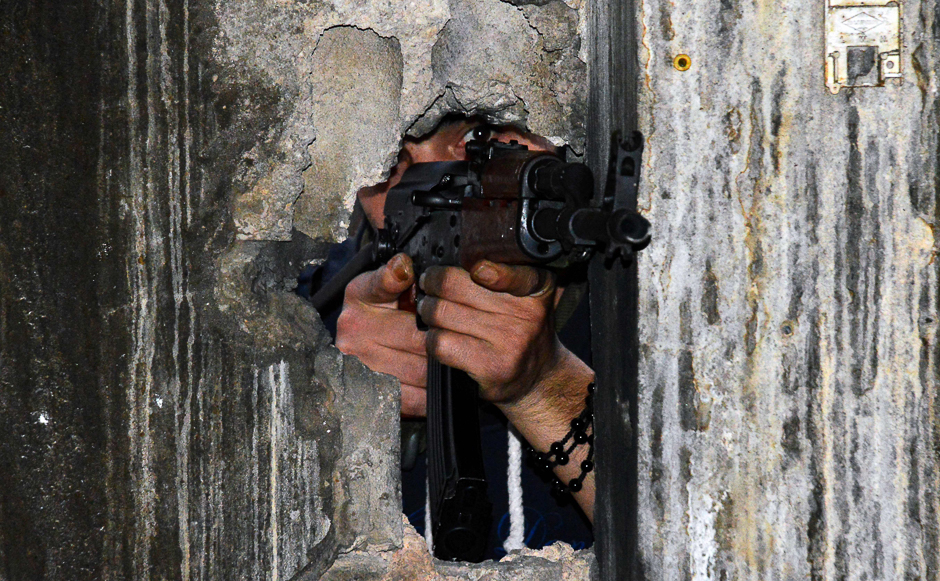 A member of the joint Palestinian security takes position through a hole in a wall with a kalashnikov assault rifle in Ain al-Hilweh camp, Lebanon's largest Palestinian refugee camp, near the southern coastal city of Sidon. PHOTO: AFP