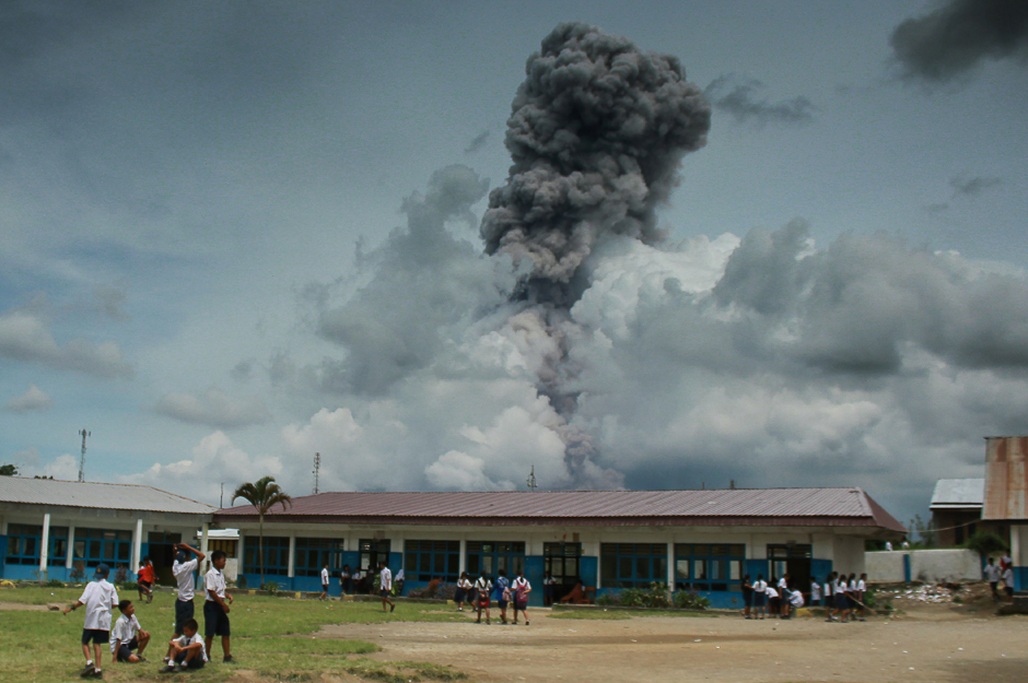 This picture taken in Karo, Nort Sumatra on April 11, 2017 shows Indonesian pupils playing with the background of Mount Sinabung volcano spewing thick smoke. PHOTO: AFP