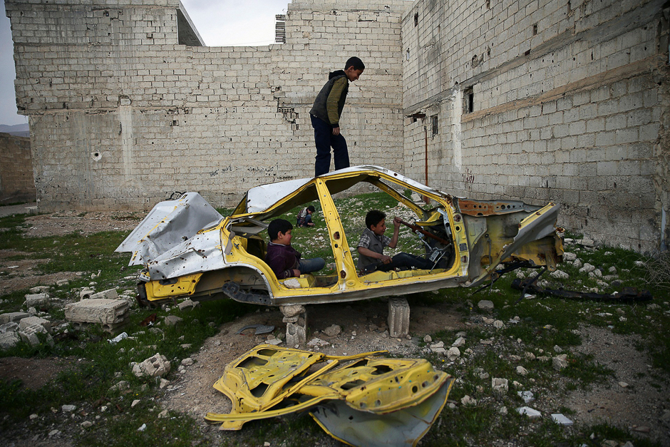 Boys play on a wrecked car in the rebel held besieged Douma neighbourhood of Damascus, Syria April. PHOTO: REUTERS