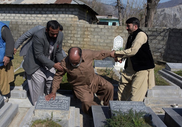 This photograph taken on February 12, 2017, shows elderly Indian Kashmiri Muhammad Ashraf (C) being helped by his son Muhammad Asghar (L) and a relative as he touches the grave of his mother at a graveyard on the outskirts of Muzaffarabad. PHOTO: AFP