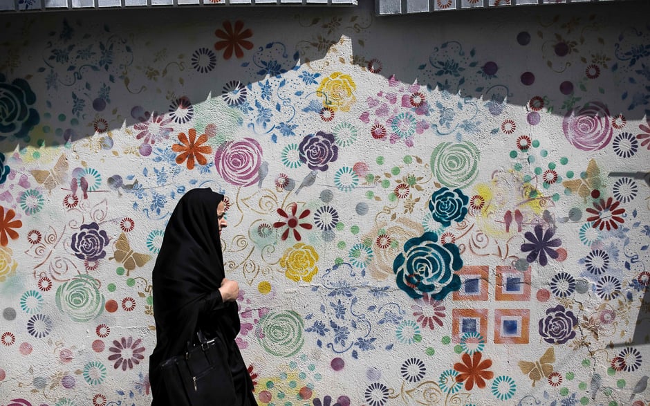 An Iranian woman walks past a graffiti in Tehran. PHOTO: AFP