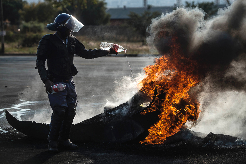 A South African policeman attempts to extinguish a fire after demonstrators burnt tyres to barricade a road, during violent protest demanding better housing on May 11, 2015 in Finetown, Ennerdale, South Africa. PHOTO: AFP