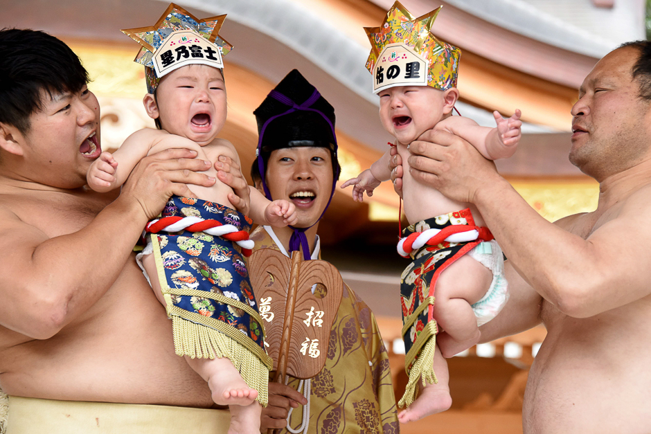 Sumo wresters hold up crying babies in front of a referee (C) clad in a traditional costume during a 