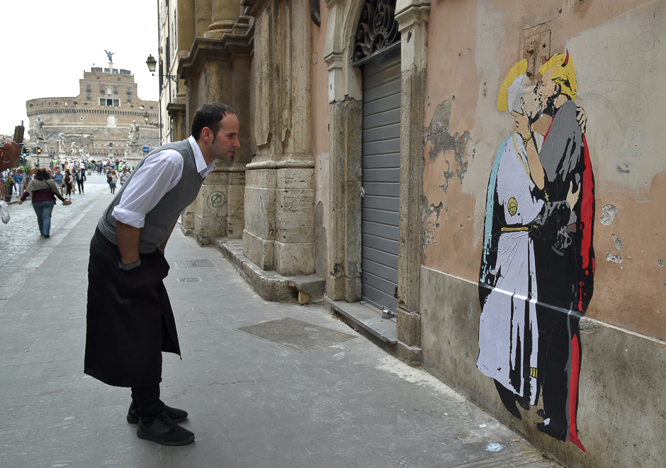 A waiter looks at a collage showing Pope Francis kissing US President Donald Trump near Castel Sant'Angelo in central Rome. PHOTO: AFP