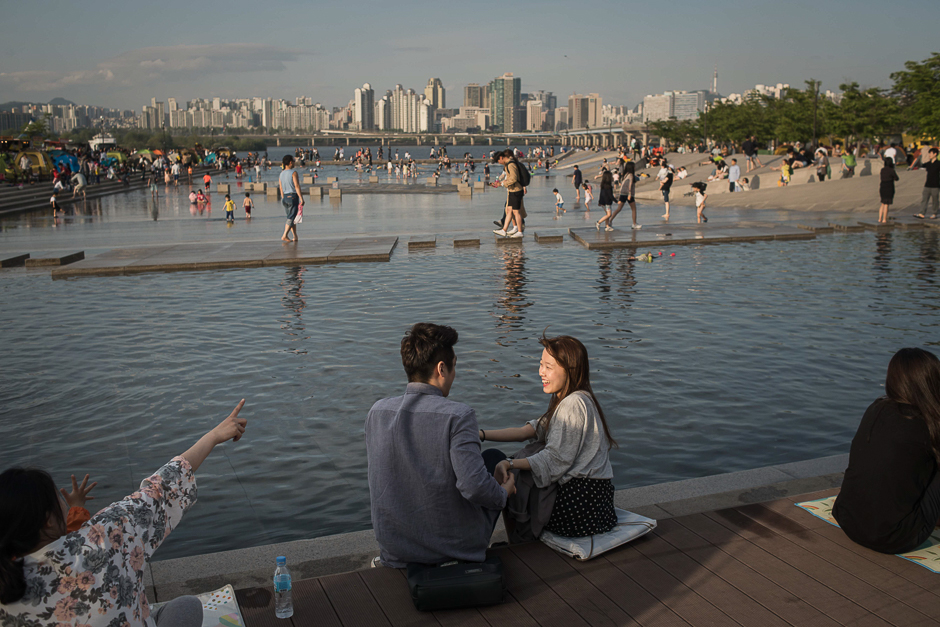 Young couples sit next to a water feature before the Han River and the city skyline, at Yeouido Park in Seoul. PHOTO: AFP