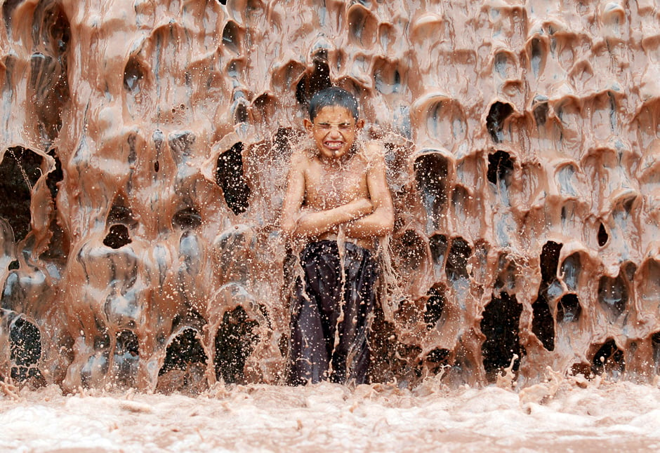 An Afghan boy cools off under a muddy waterfall on the outskirts of Jalalabad province, Afghanistan. PHOTO: REUTERS